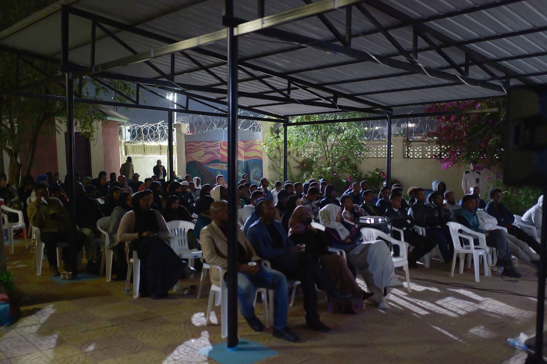 The courtyard full of people watching the screen under the roof at night