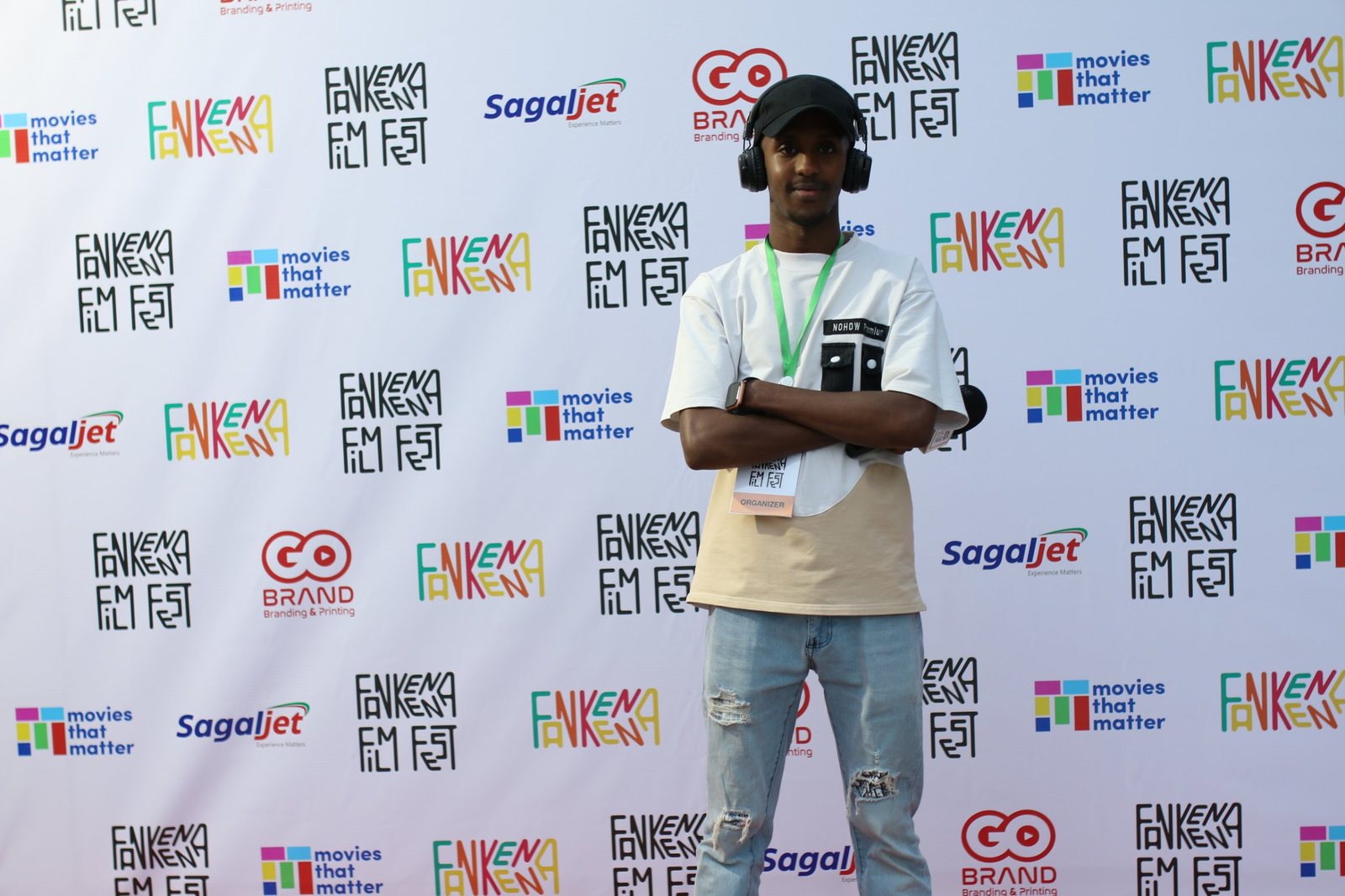 A festival organiser with headphones and an organiser badge in front of the sponsor wall