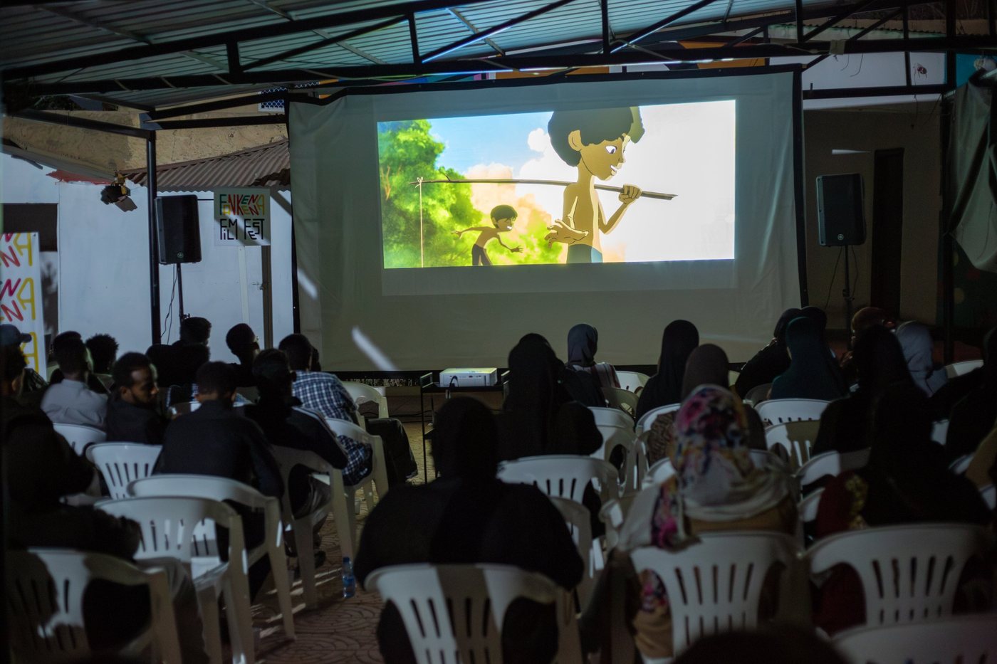 The audience watches an animated film under the courtyard roof