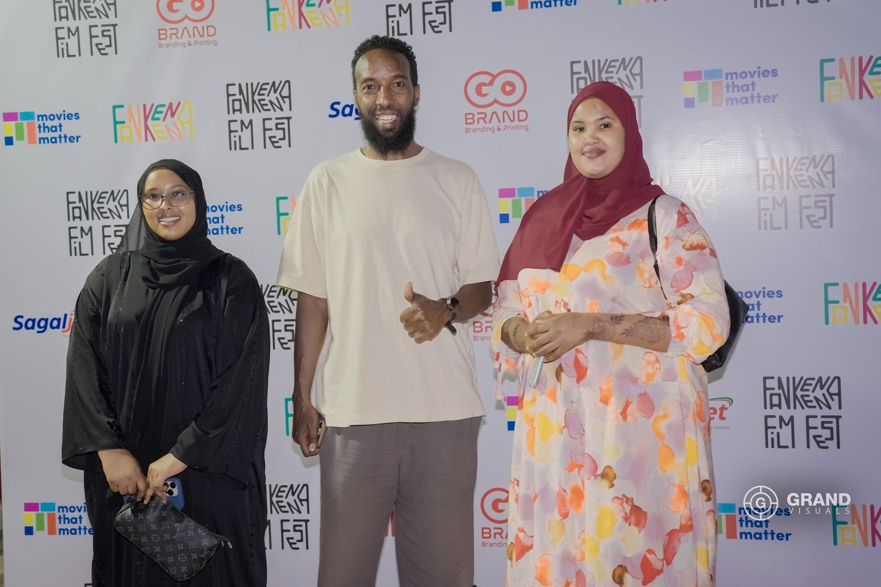 Three guests smile on the red carpet in front of the festival wall