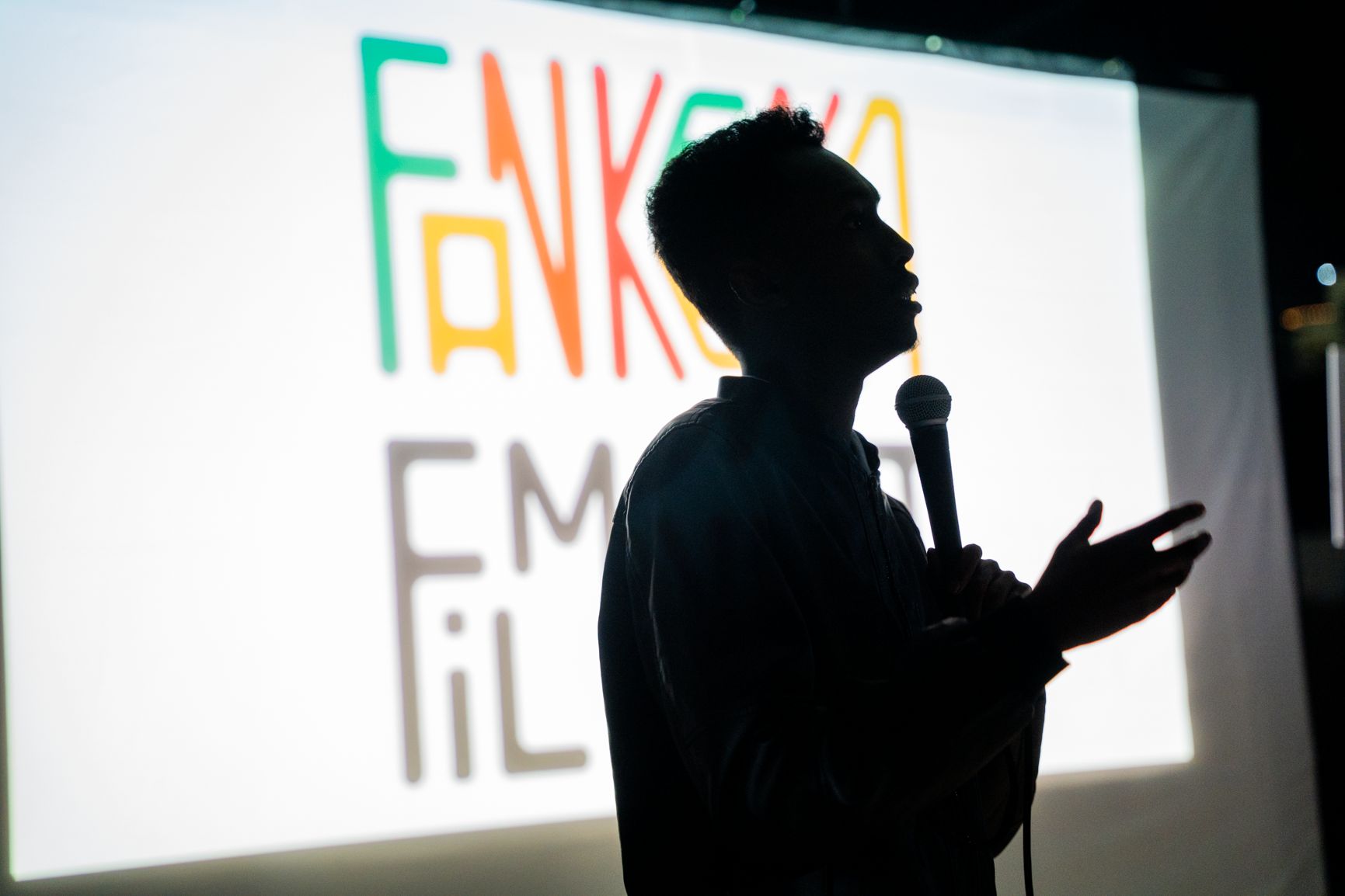 A speaker in silhouette in front of the festival logo on the screen